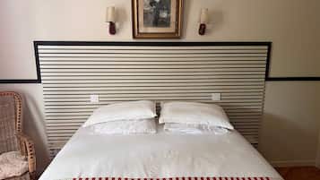 Ein Bett mit weißen Leinentüchern und einer gestreiften roten und weißen Decke, ein Kopfteil mit horizontalen Linien sowie zwei an der Wand befestigte Lampen.