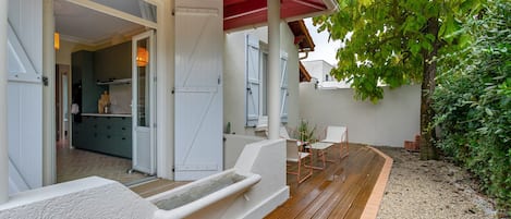 A covered outdoor area with a wooden deck, a seating arrangement, and a view of a building with a red roof.