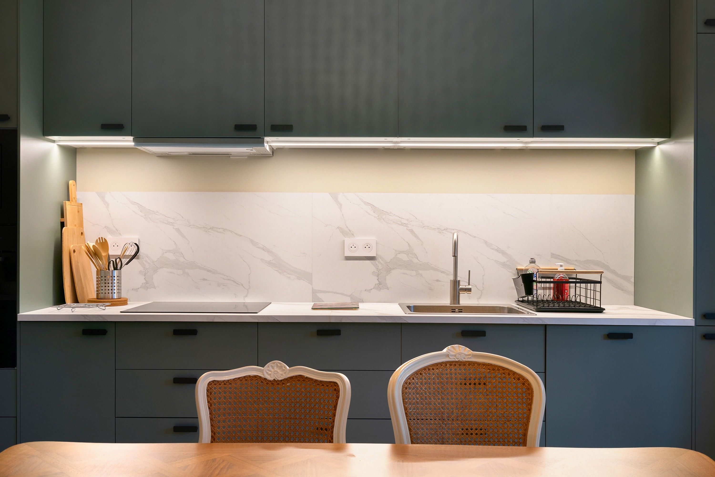 Cocina moderna con salpicadero de mármol, pileta de acero inoxidable y un comedor con dos sillas.
