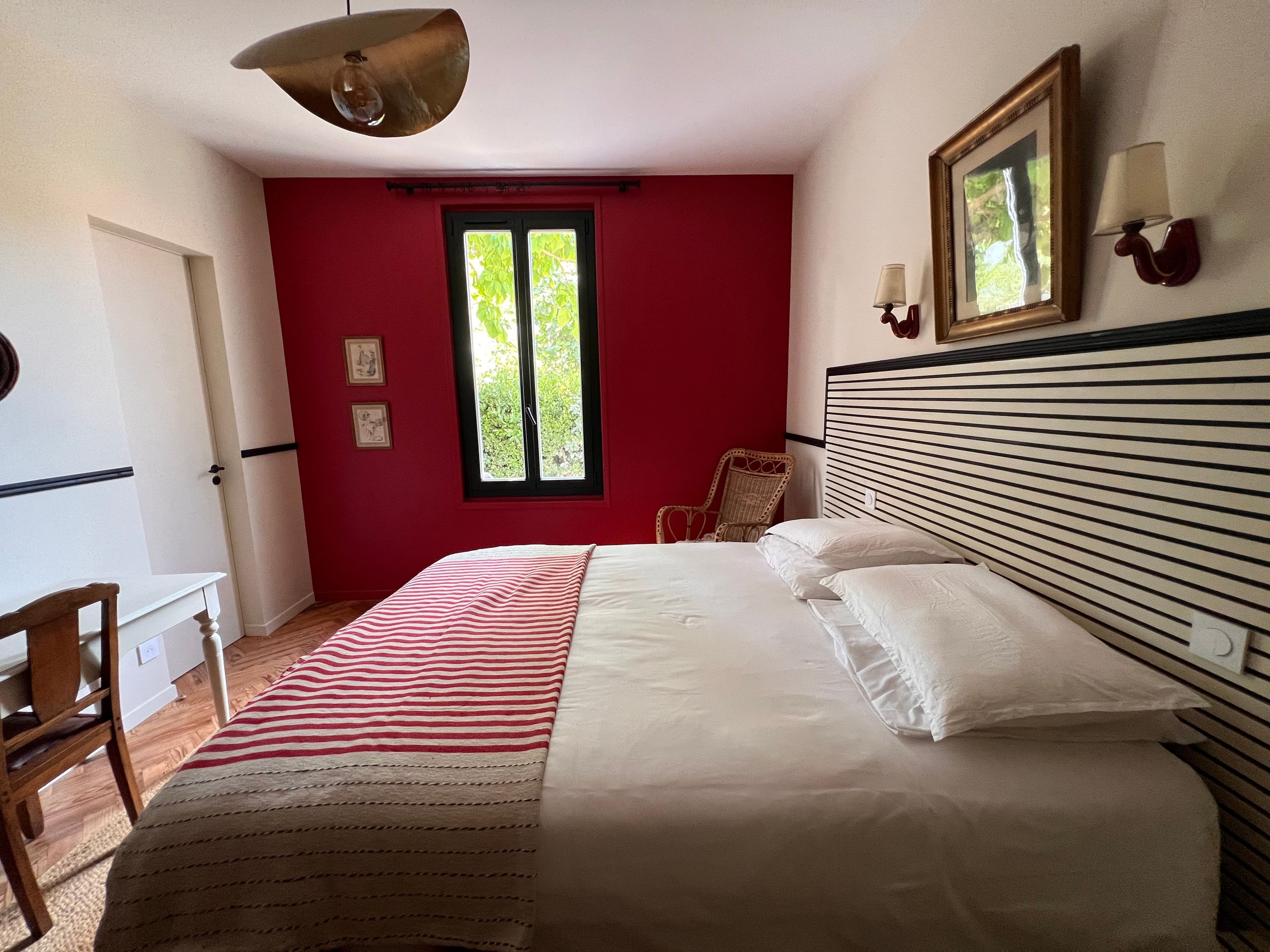 Een slaapkamer met een bed, een stoel, een bureau, een raam en een wandlamp.