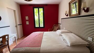 Een slaapkamer met een bed, een stoel, een bureau, een raam en een wandlamp.