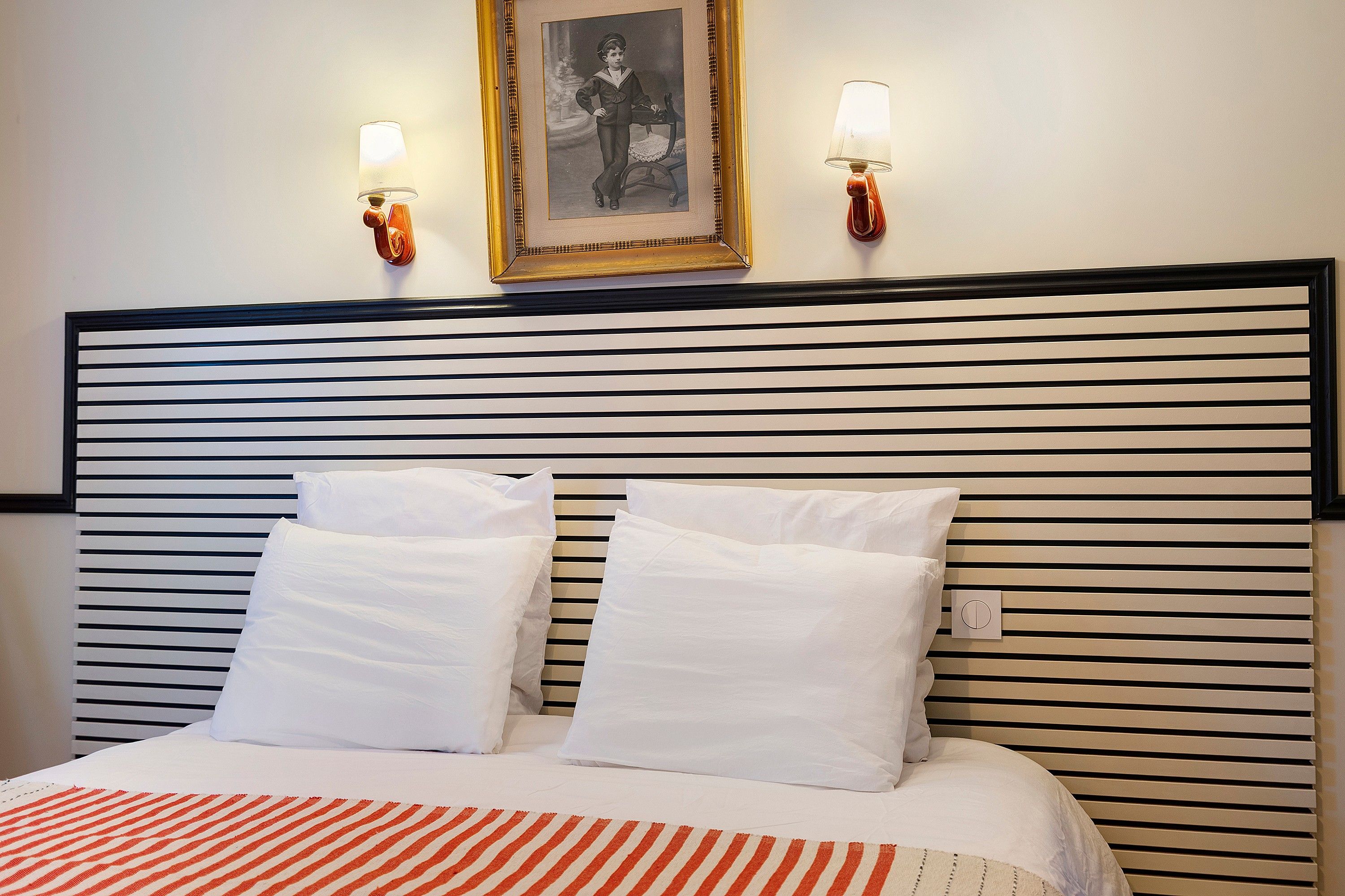 Ein Hotelzimmer mit einem gestreiften Kopfteil, zwei weißen Kissen, einer gestreiften Decke und zwei Wandlampen.
