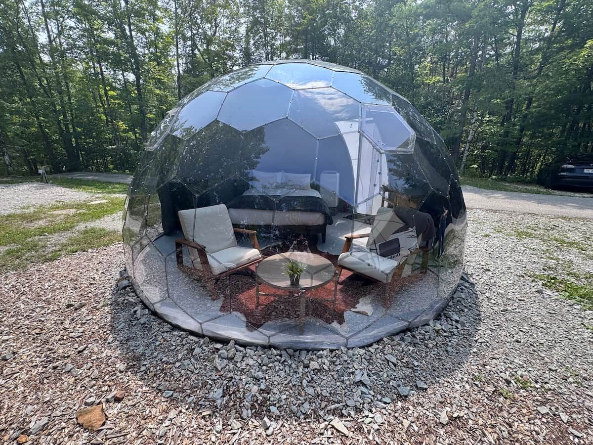 A geodesic dome structure with a seating area inside, surrounded by gravel and trees.