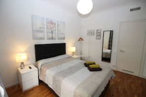 A bedroom with a bed, bedside tables, a nightstand, a mirror, and wall art. - Habitaciones en Bonito Toledo (Madrid)