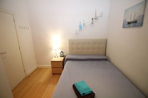 A small, neatly arranged bedroom with a single bed, a bedside table with a lamp, and a wall-mounted shelf with decorative items. - Habitaciones en Bonito Toledo (Madrid)