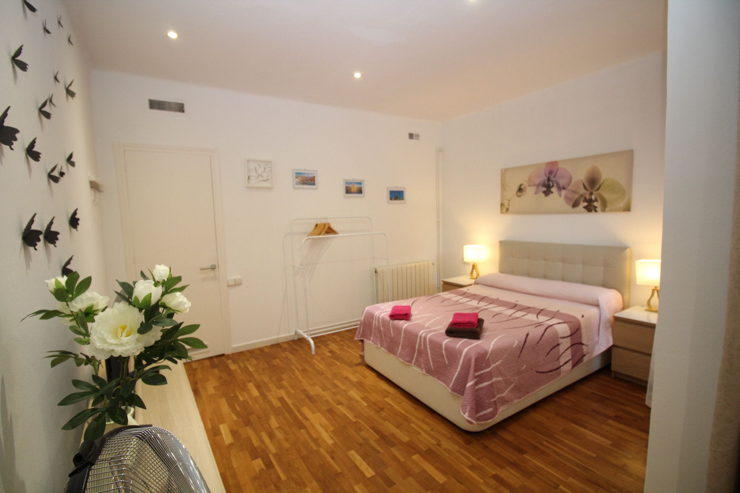 Un dormitorio con cama, mesitas de noche, radiador, estante en la pared y un cuadro.