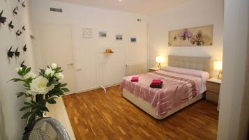 Un dormitorio con cama, mesitas de noche, radiador, estante en la pared y un cuadro.