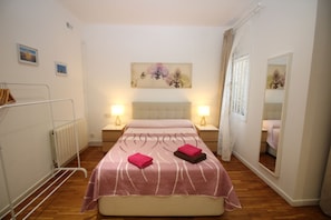 A hotel room with a double bed, two bedside tables with lamps, a radiator, a mirror, and a painting on the wall. - Habitaciones en Bonito Toledo (Madrid)