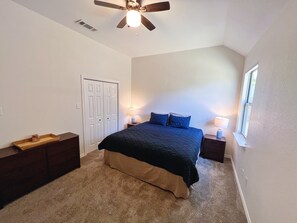 Ein Schlafzimmer mit einem Bett, zwei Nachttischen, einem Deckenventilator, einem Fenster und einer Tür.