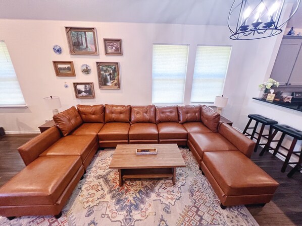 A living room with a brown leather sectional sofa, a wooden coffee table, patterned rug, and framed pictures on the wall. - The Blue Cottage- 3BR Family Retreat on Lake Granbury, Gated, Community Pool (Granbury)