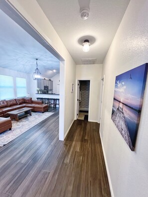 A spacious living area with a sectional sofa, a wooden floor, and a view of the kitchen. - The Blue Cottage- 3BR Family Retreat on Lake Granbury, Gated, Community Pool (Granbury)