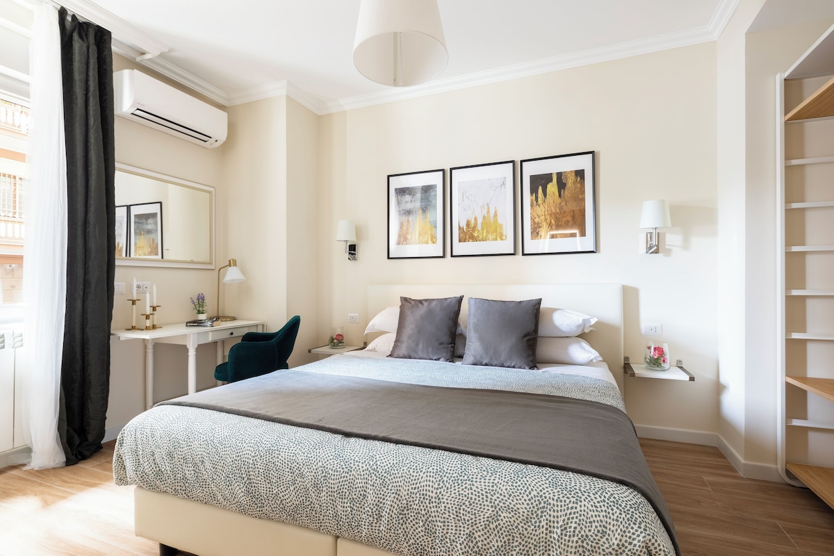 Une chambre d’hôtel comprenant un lit, des tables de chevet, un bureau, une chaise, un miroir et des œuvres d’art accrochées au mur.