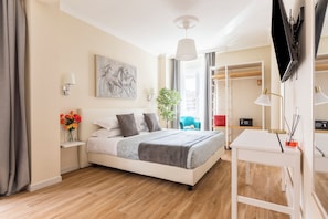 Une chambre à coucher moderne, avec un lit, des tables de chevet, un bureau, une chaise, une plante et un téléviseur fixé au mur.
