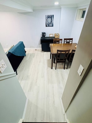 Ein Essbereich mit einem Holztisch und Stühlen, einem schwarzen Schrank mit Wasserkocher und einem gerahmten Bild an der Wand.