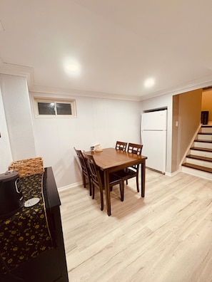 Ein Essbereich mit Holztisch und Stühlen, einem Kühlschrank und einer Treppe, die zu einer weiteren Ebene führt.