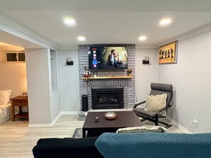 Ein Wohnzimmer mit Kamin, einem darüber angebrachten Fernseher, einer Couch, einem Couchtisch und einem Sessel.