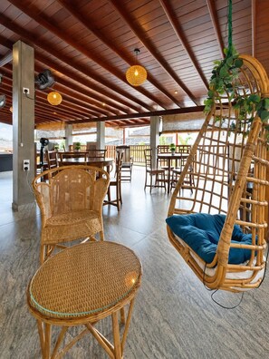 A spacious indoor area with wooden ceiling beams, wicker furniture, and hanging plants. - Keanu Resort  (Ambalangoda)
