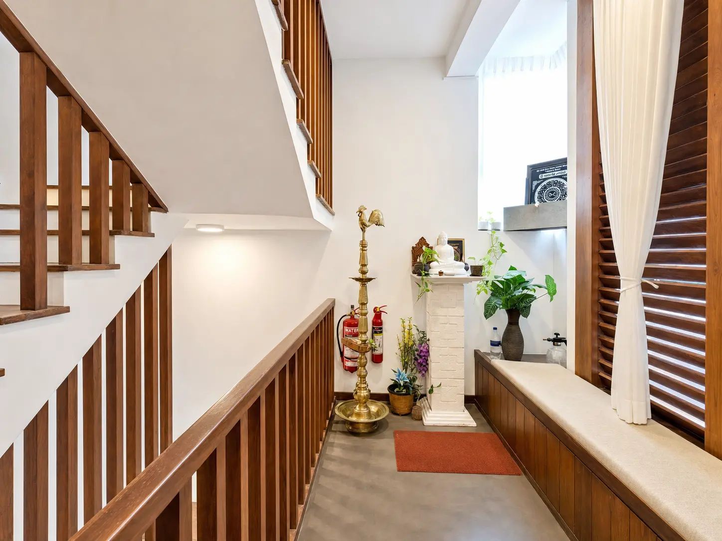 Un escalier avec des rampes en bois mène à un palier doté d’un mur blanc, d’une petite étagère ornée d’objets décoratifs et d’une plante en pot.