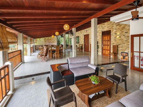 Un amplio espacio interior con techo de madera, una zona de estar con sofás y sillones, y una pared de piedra.