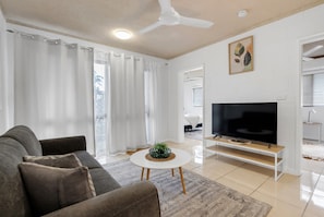 A modern living room with a sectional sofa, a flat-screen TV, and a coffee table with a plant. - Bright 2-bed Apartment Near Cairns Esplanade (Cairns)