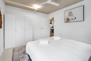A bedroom with a bed, a ceiling fan, a white door, and a framed picture on the wall. - Bright 2-bed Apartment Near Cairns Esplanade (Cairns)