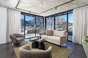 A modern living room with a sofa, two armchairs, a coffee table, and a view of a mountain and cityscape through large windows. - FortyOnL | Stunning City and Table Mountain Views (Cape Town)