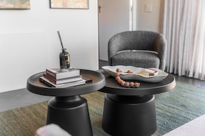 A modern living room with two black round tables, one with books and a perfume bottle, and the other with a plate of snacks. - FortyOnL | Stunning City and Table Mountain Views (Cape Town)