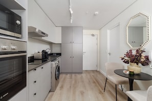 A modern kitchen with Bosch appliances, a washing machine, and a dining area with a round table and chair. - Stylish City Escape | Rooftop Pool and Gym (Cape Town)