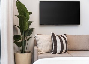 A living room with a flat-screen TV mounted on the wall, a beige sofa with striped pillows, and a large potted plant. - Stylish City Escape | Rooftop Pool and Gym (Cape Town)