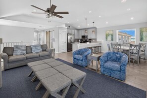 A modern living room with a sofa, ottoman, and chairs, a kitchen with a central island, and a dining area with a table and chairs. - Fluorescent Beauty 4BR Home (Port Aransas)