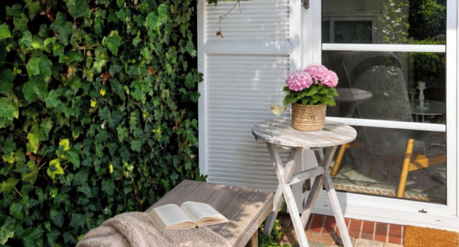 A small outdoor seating area with a table and a bench, a potted plant, and an open book on the bench.