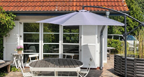 A covered outdoor seating area with a table and chairs, a potted plant, and a car parked in the background. - Holiday Home 'Natürlich Am Bodden' with Lake View, Private Terrace and Wi-Fi (Fuhlendorf)