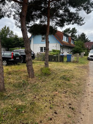 Un quartier résidentiel avec une maison, des voitures garées et un chemin de terre.