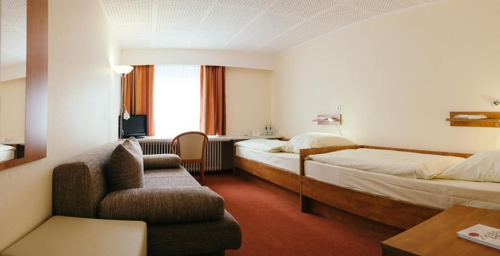 A hotel room with a single bed, a sofa, a desk, and a chair.