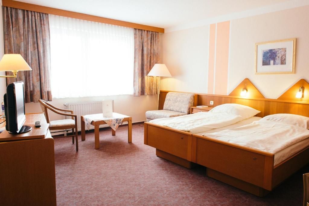 Une chambre d’hôtel comprenant un lit, des lampes de chevet, un bureau avec une chaise, une télévision et une fenêtre avec des rideaux.
