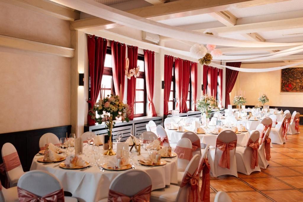 Una sala de banquetes amb taules rodones preparades per a un esdeveniment formal, amb tovallons blancs i cadires amb lazos roses.