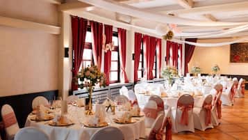 Una sala de banquetes amb taules rodones preparades per a un esdeveniment formal, amb tovallons blancs i cadires amb lazos roses.