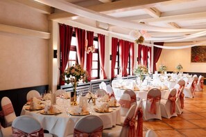 A banquet hall with round tables set for a formal event, featuring white tablecloths and chairs with pink sashes. - Hotel Daub  (Bremervörde)
