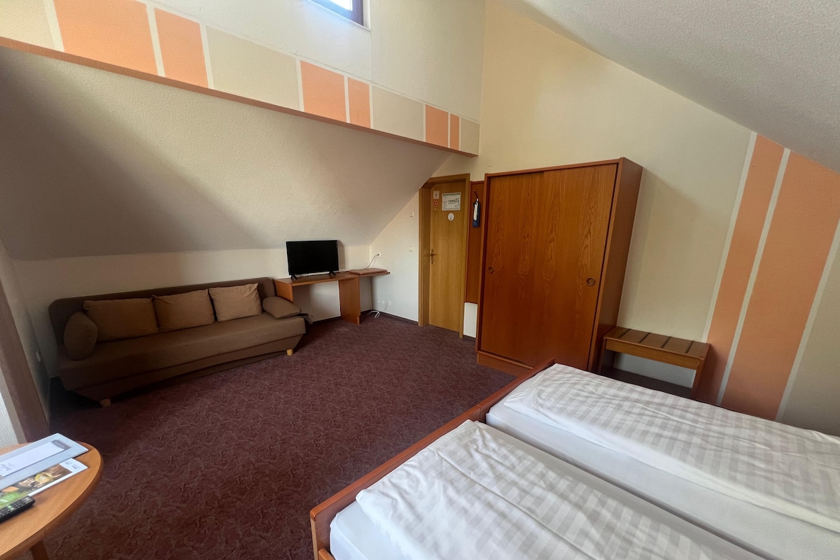 Quarto com sofá, duas camas, televisão, guarda-roupa e secretária.