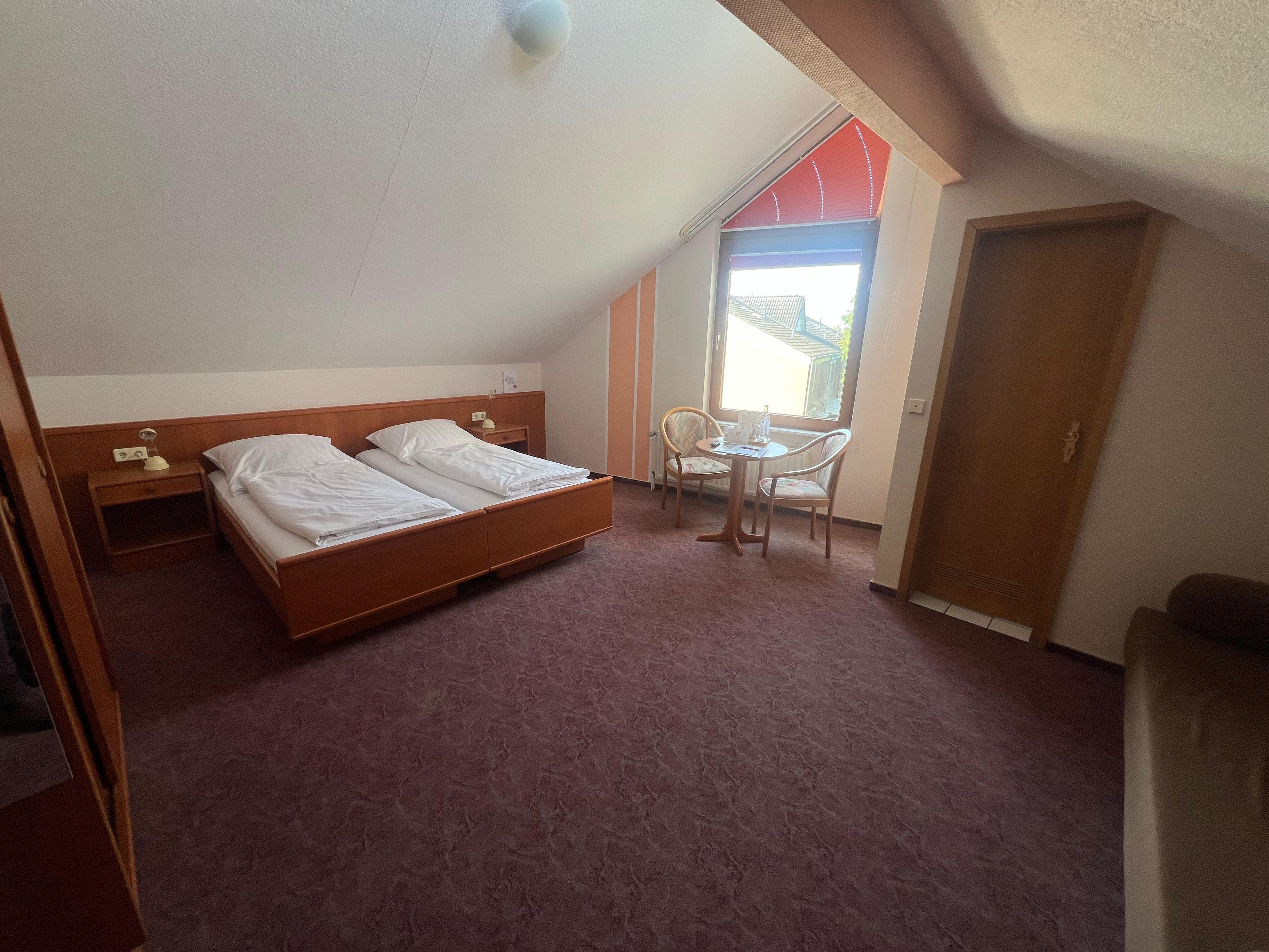 Een slaapkamer met een bed, nachtkastje, stoel en een raam.