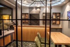 A reception area with a wooden counter, a green upholstered chair, and a wooden table. - Hotel Daub  (Bremervörde)