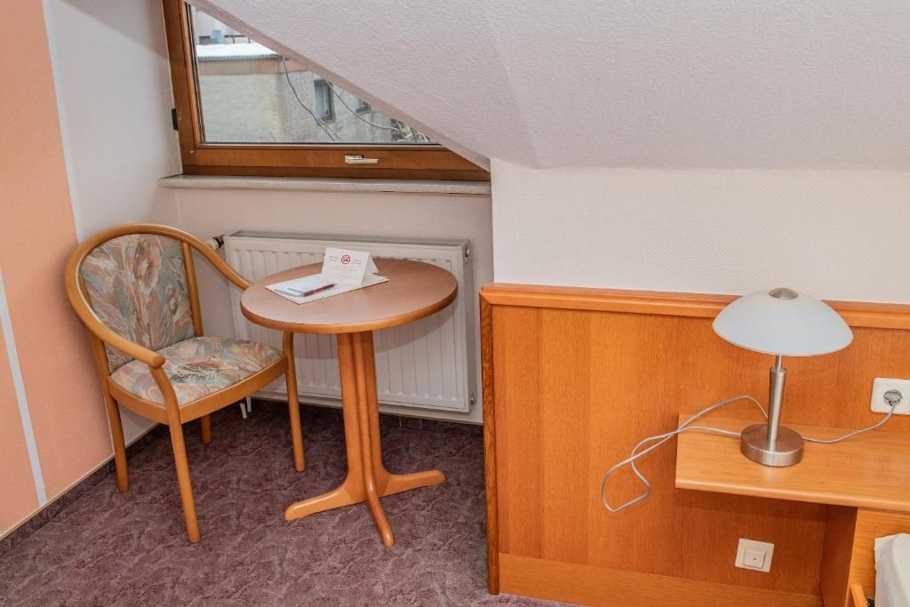Habitació petita amb una cadira de fusta, una taula rodona, una làmpada i un radiador.