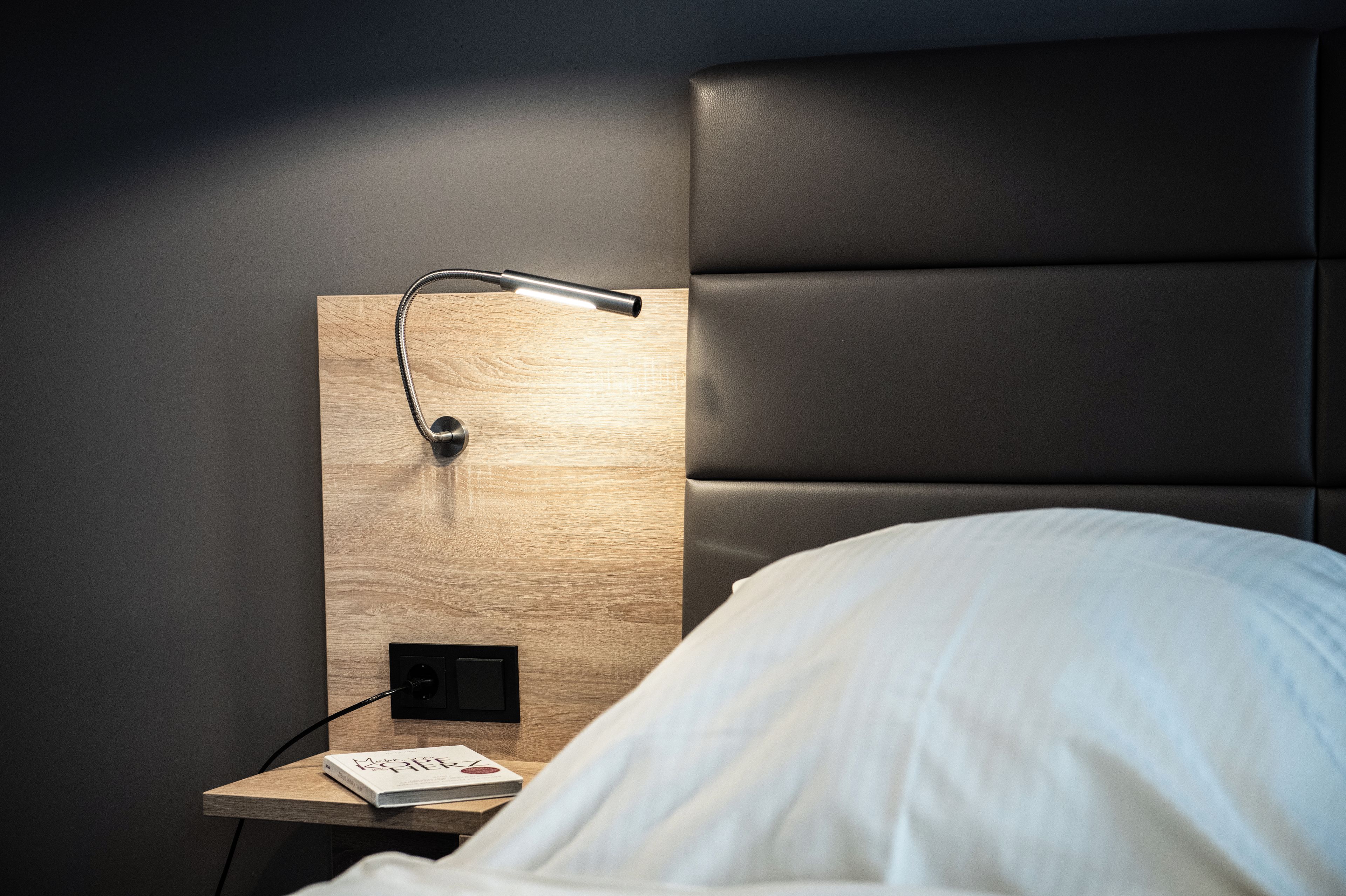 Un letto rifatto con copriletto bianco, un comodino in legno con una lampada e un libro intitolato 'The Kelp Forest'.