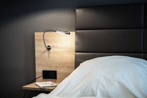 A neatly made bed with a white comforter, a wooden bedside table with a lamp, and a book titled 'The Kelp Forest'.