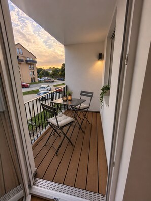A balcony with a table and chairs, a potted plant, and a view of a parking lot and buildings. - Modern worker's apartment with a balcony in Bestensee (Bestensee)
