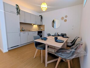 A modern kitchen with white cabinets, a wooden dining table, and a hanging light fixture. - Modern worker's apartment with a balcony in Bestensee (Bestensee)