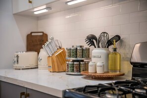 Uma bancada de cozinha com diversos utensílios, um porta-temperos, um saleiro e pimenteiro, e uma garrafa de óleo.
