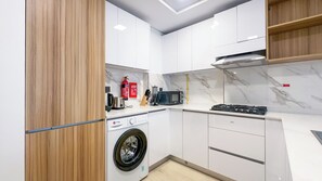A compact kitchen with a washing machine, microwave, and stove. - Modern 1BR apartment in Elysee 3 by Pantheon, Pool & Gym access (Dubai)