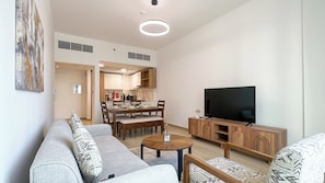 A modern living room with a sofa, coffee table, TV, and dining area. - Modern 1BR apartment in Elysee 3 by Pantheon, Pool & Gym access (Dubai)
