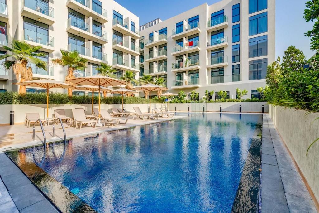 A modern hotel with a swimming pool, sun loungers, and palm trees.